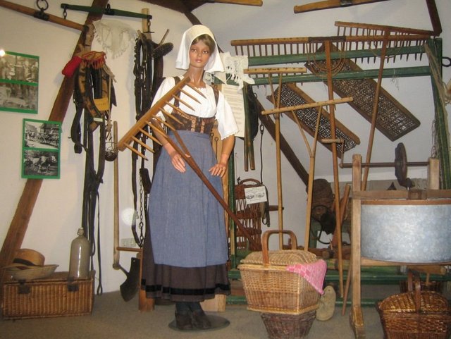 Ein Ausstellungsraum des Heimatmuseums. Darauf zu sehen ist eine altertümlich gekleidete Puppe mit historischen landwirtschaftlichen Werkzeugen.